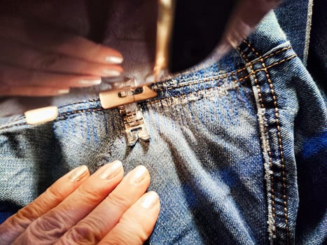 Sewing machine and blue jeans fabric. A woman's hand and fingers next to a sewing machine needle when sewing up tear in denim