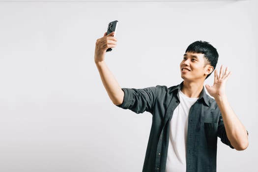 Portrait of a cheerful Asian young man taking a selfie with his smartphone, capturing his excitement in a studio shot isolated on white. Fun with photography