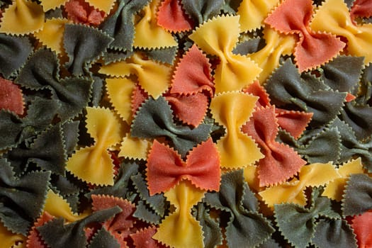 Uncooked Vibrant Colored Farfalle Pasta: A Culinary Canvas of Multicolored Bow-Tie Macaroni, Creating a Lively and Textured Background for Gourmet Cooking Enthusiasts. Colored Dry Pasta. Raw Macaroni