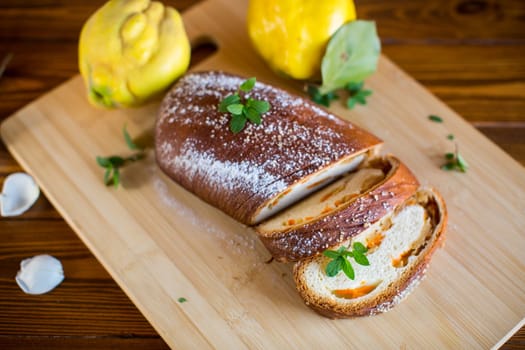 Cooked sweet pie with quince and pumpkin inside, yeast dough roll, on a wooden table.