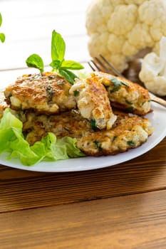 cooked vegetarian fried cauliflower cutlets, in a plate on a wooden table.