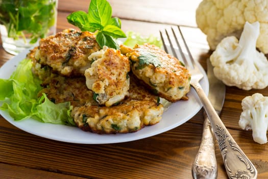 cooked vegetarian fried cauliflower cutlets, in a plate on a wooden table.