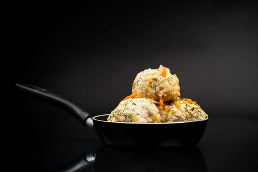 cooked chicken diet meatballs in a frying pan, isolated on a black background