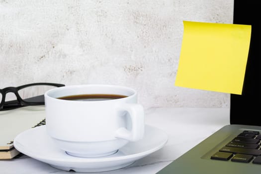 Yellow sticky note on a notebook with coffee, notepad and reading glass. Copy space.