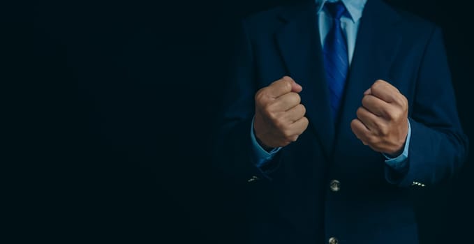 Businessman in a suit stands and makes a fist gesture on a dark background.