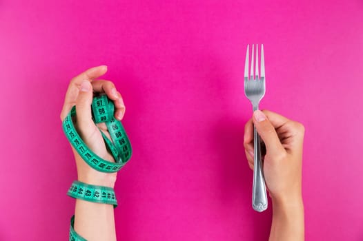 Close-up of a hand with a measuring tape wrapped around it and a fork in the other hand. Diet and healthy eating concept.