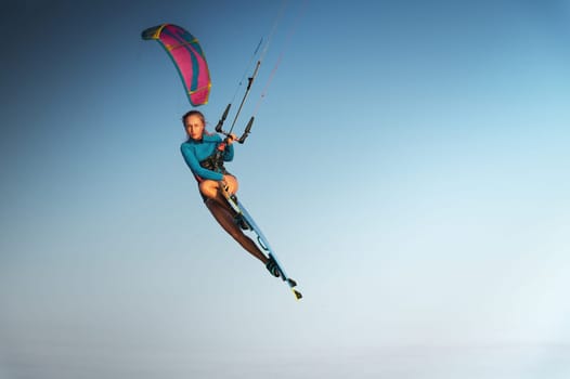 Caucasian woman kitesurfer athlete doing a trick in the air against a blue sky without a cloud. Professional kitesurfing training.