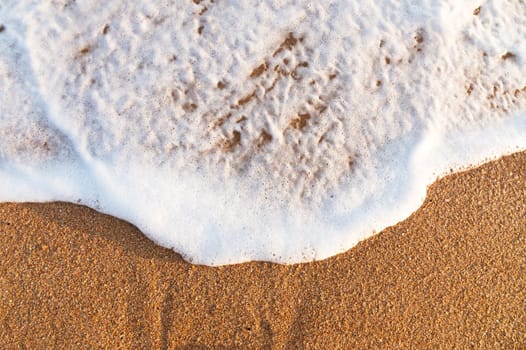 Beach sand, sea water, summer background. Sandy beach texture. White foam wave, top view of the sandy seashore.
