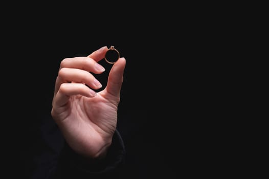 Diamond ring in the hand of a young woman on a black background. Concept of love and wedding or divorce and unsuccessful marriage.