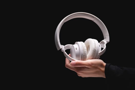 Wireless headphones on a black background. White full-size noise-canceling headset with built-in microphone. Side view of acoustic stereo sound system in female hand.