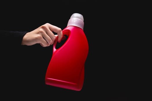 Close-up of a woman's hand holding household chemicals, on a black background with copy space. Advertisement, best detergent, cleaner, all-purpose cleaner or laundry detergent.