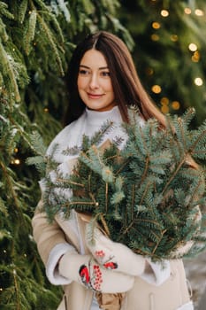 A girl with long hair in winter on the street with a bouquet of fresh fir branches.