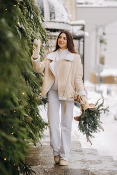 A girl with long hair in winter on the street with a bouquet of fresh fir branches.