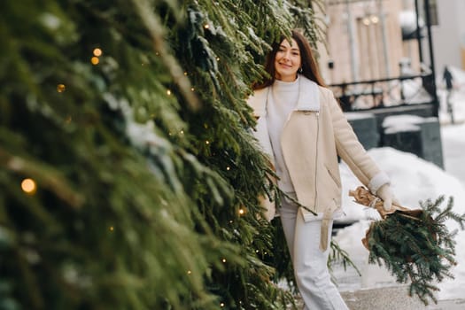 A girl with long hair in winter on the street with a bouquet of fresh fir branches.