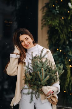 A girl with long hair in winter on the street with a bouquet of fresh fir branches.