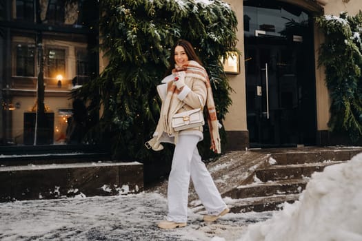 A girl with long hair in a scarf and with a white handbag walks down the street in winter.