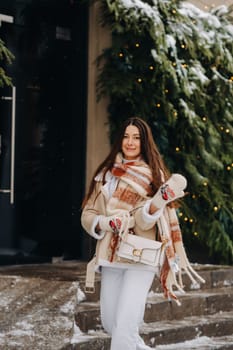 A girl with long hair in a scarf and with a white handbag walks down the street in winter.