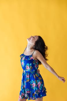 Portrait of a beautiful woman in a blue summer dress with flowers on a yellow background