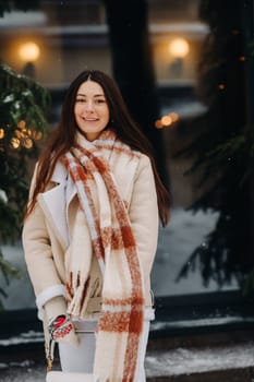 A girl with long hair in a scarf and with a white handbag walks down the street in winter.