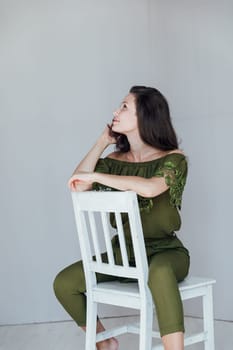 Portrait of a beautiful woman in green clothes on a white chair