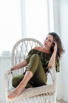 Portrait of a brunette woman in green clothes on a white chair