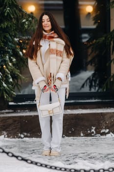 A girl with long hair in a scarf and with a white handbag walks down the street in winter.