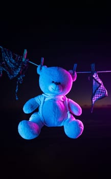 teddy bear toy hangs on a clothesline on clothespins in neon light. tied with shibari ropes