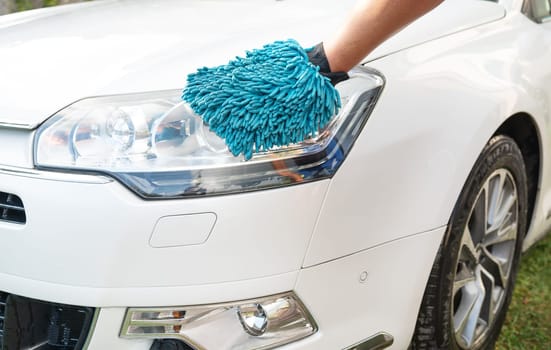 Hand in blue microfiber glove cleaning a white car s headlight