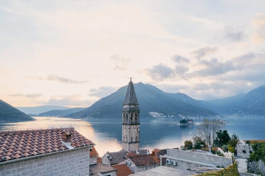 Bell tower of the Church of St. Nicholas over the roofs of old houses against the backdrop of the mountains in the evening. Montenegro. High quality photo