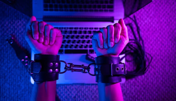 the female sexy hands in bdsm handcuffs with laptop in neon light on dark background