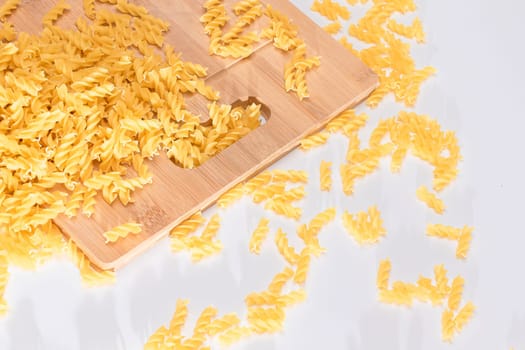 Uncooked Fusilli Pasta Scattered on Wooden Board and White Table. Raw and Dry Macaroni. Fat and Unhealthy Food