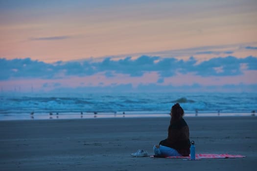 Velsen-Noord, Netherlands, August 30, 2023: Girl meditating on the beach at sunset in the Netherlands.