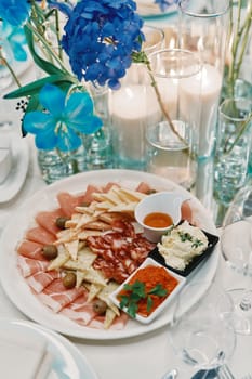 Snacks lie on a plate near a bouquet of flowers on a set table. High quality photo