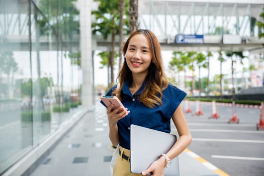 A curly-haired woman in a blue shirt stands on a city street, engrossed in her phone. She is browsing social media, connected to the world around her.