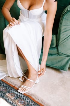 Bride fastens her high-heeled shoes while sitting in a chair. Cropped. Faceless. High quality photo