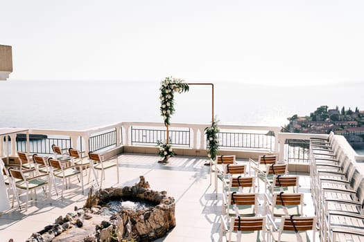 Rows of chairs stand near a fountain in front of a wedding arch on a terrace above the island of Sveti Stefan. Montenegro. High quality photo