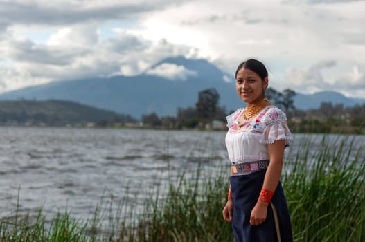 copy space of young indigenous woman on the shore of a lake with traditional dress from her culture of Ecuador with the Imbabura volcano erupting in the background. High quality photo