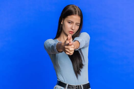 Caucasian young woman pointing around with finger gun gesture, looking confident, making choice shooting killing with hand pistol right on target. Girl isolated on blue wall background. Advertisement