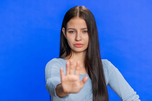 Come here, join us. Welcome. Brunette attractive woman showing inviting gesture with hands, ask to join, beckoning to coming, gesturing hello, goodbye. Strict girl isolated on blue studio background