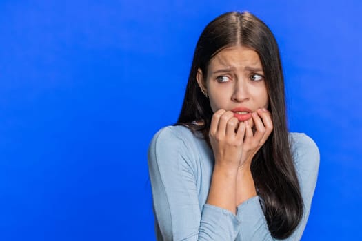 Stressed shocked depressed Caucasian young woman terrified about danger problems, suffering phobia, anxiety disorder, expresses fear, insecure, stress, panic. Scared fearful girl on blue background