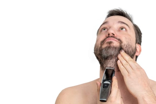 Close-up of a young man using an electric razor to shave his beard, against a white background. The man is carefully grooming his facial hair with a modern grooming tool.