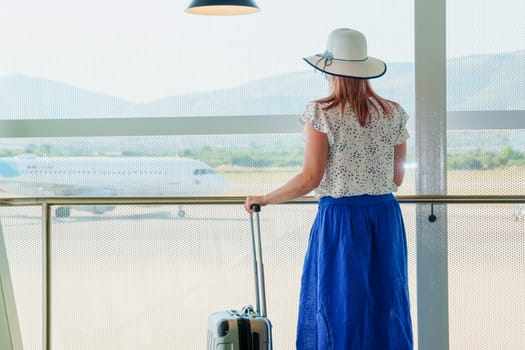 A young girl standing by a wide airport window, looking out at the runway and reflecting on her upcoming vacation. The natural light creates a serene atmosphere as the girl gazes outside.