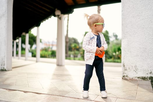 Little girl in sunglasses stands half-turned in a gazebo in the garden. High quality photo