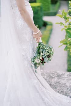 Bride with a bouquet stands half-turned in the park. Side view. Cropped. High quality photo