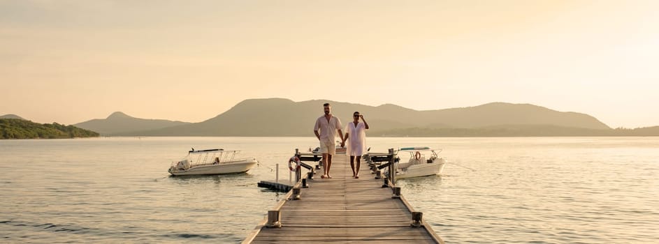 A couple of European men and an Asian woman on vacation in Thailand walking at a wooden pier in the ocean during sunset in Samaesan Sattahip Thailand