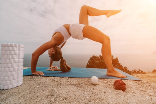 Middle aged well looking woman with black hair doing Pilates with the ring on the yoga mat near the sea on the pebble beach. Female fitness yoga concept. Healthy lifestyle, harmony and meditation.