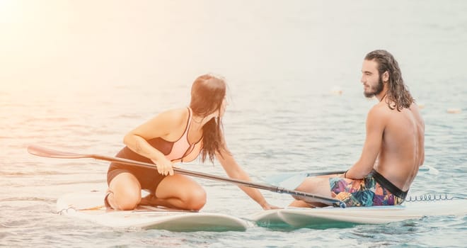 Sea woman and man on sup. Silhouette of happy young woman and man, surfing on SUP board, confident paddling through water surface. Idyllic sunset. Active lifestyle at sea or river