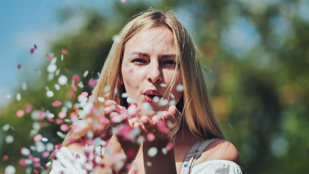 A girl blows a multi-coloured paper confetti out of her hands