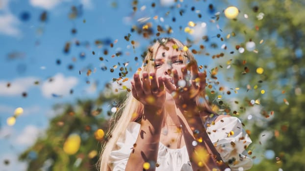 The girl blows a golden confetti out of her hands