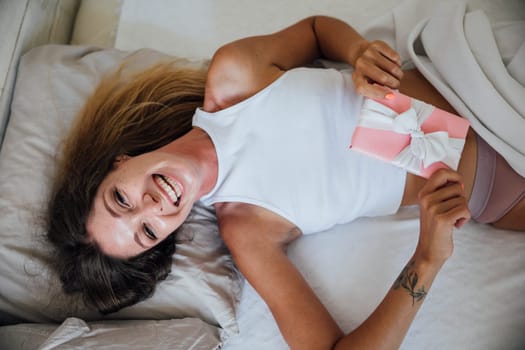Beautiful young woman in bedroom on bed received holiday gift